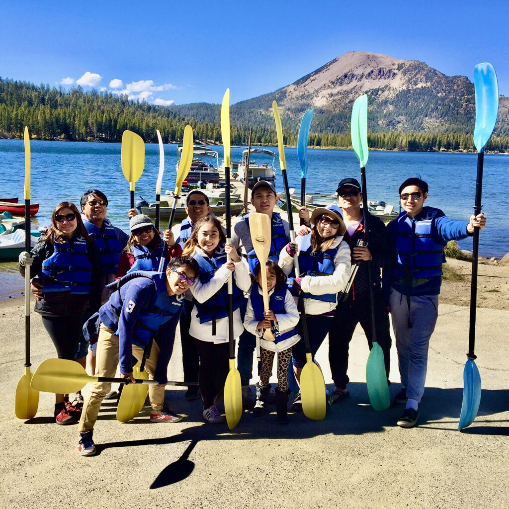 Photo of a group of people holding kayak paddles and standing in front of a lake