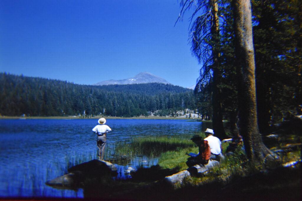 A photo from the 1960s of three people with their backs to the camera looking out on the lake and mountains