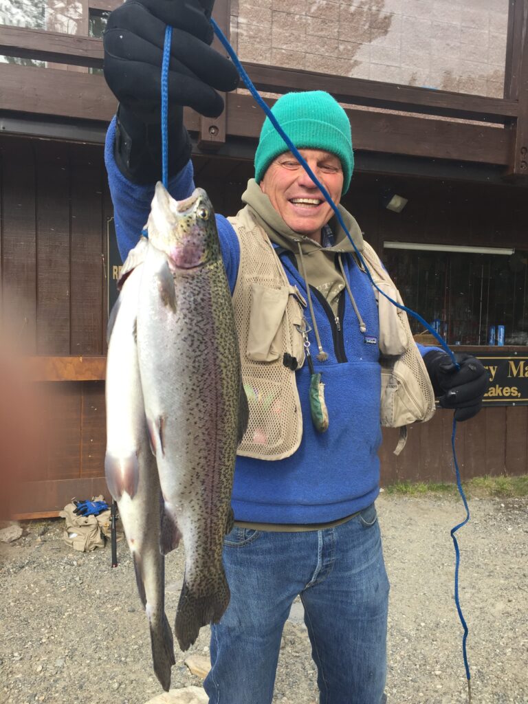 A photo of a man wearing a beanie holding a stringer of two trout