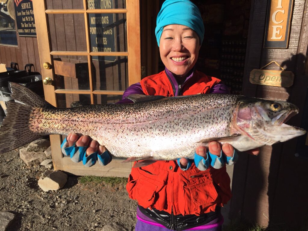 A woman holding a large rainbow trout and smiling