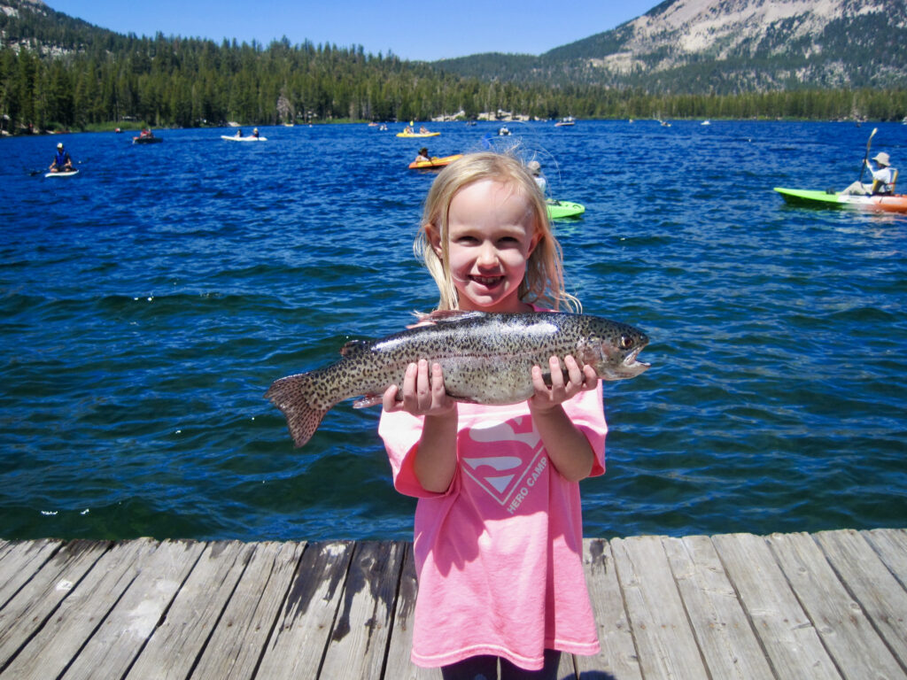 Photo of a young girl standing on a dock holding a small rainbow trout